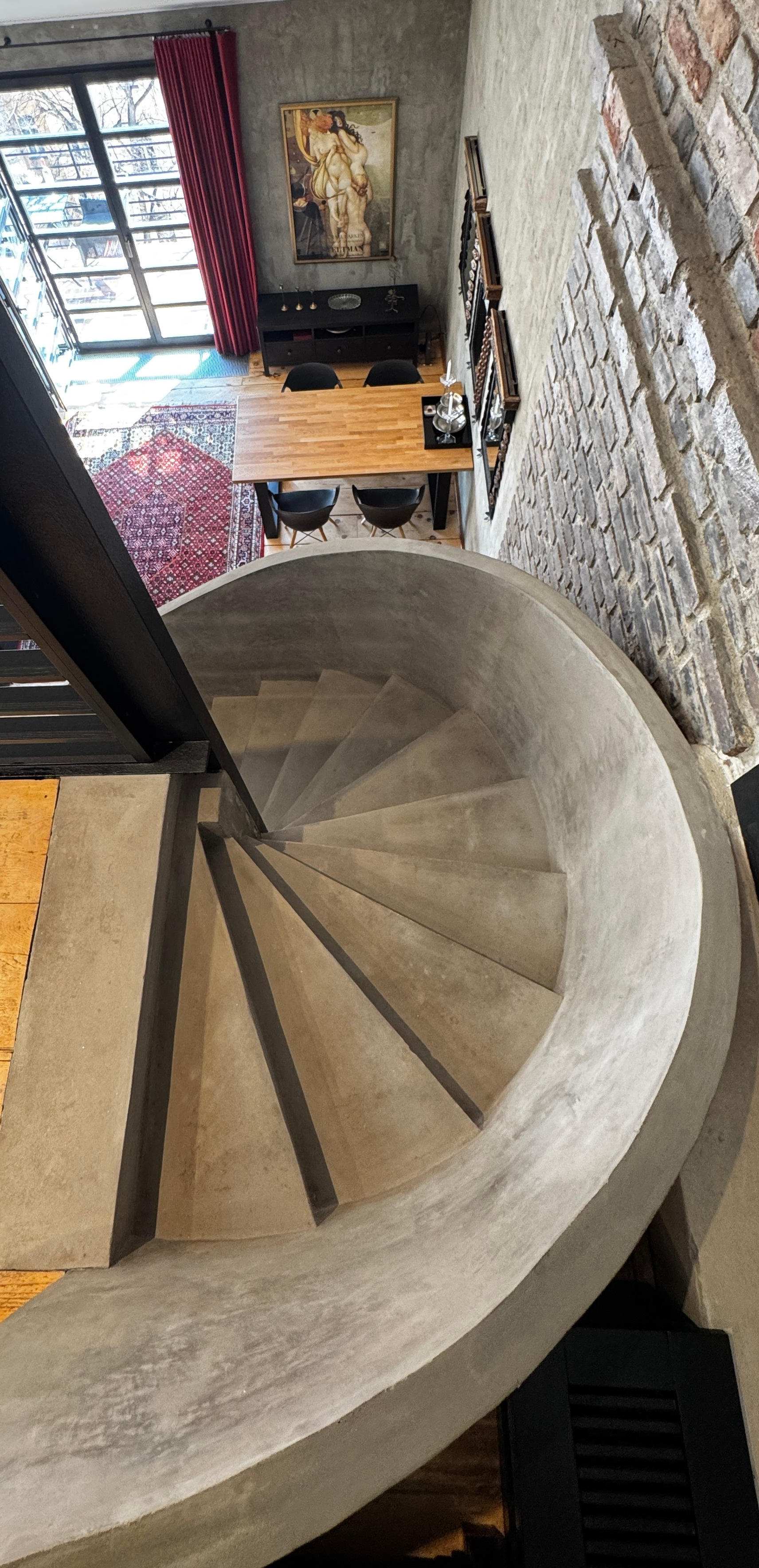 Sculptural concrete spiral staircase at Polska Penthouse ascending to the atelier mezzanine — a defining architectural feature of the triplex