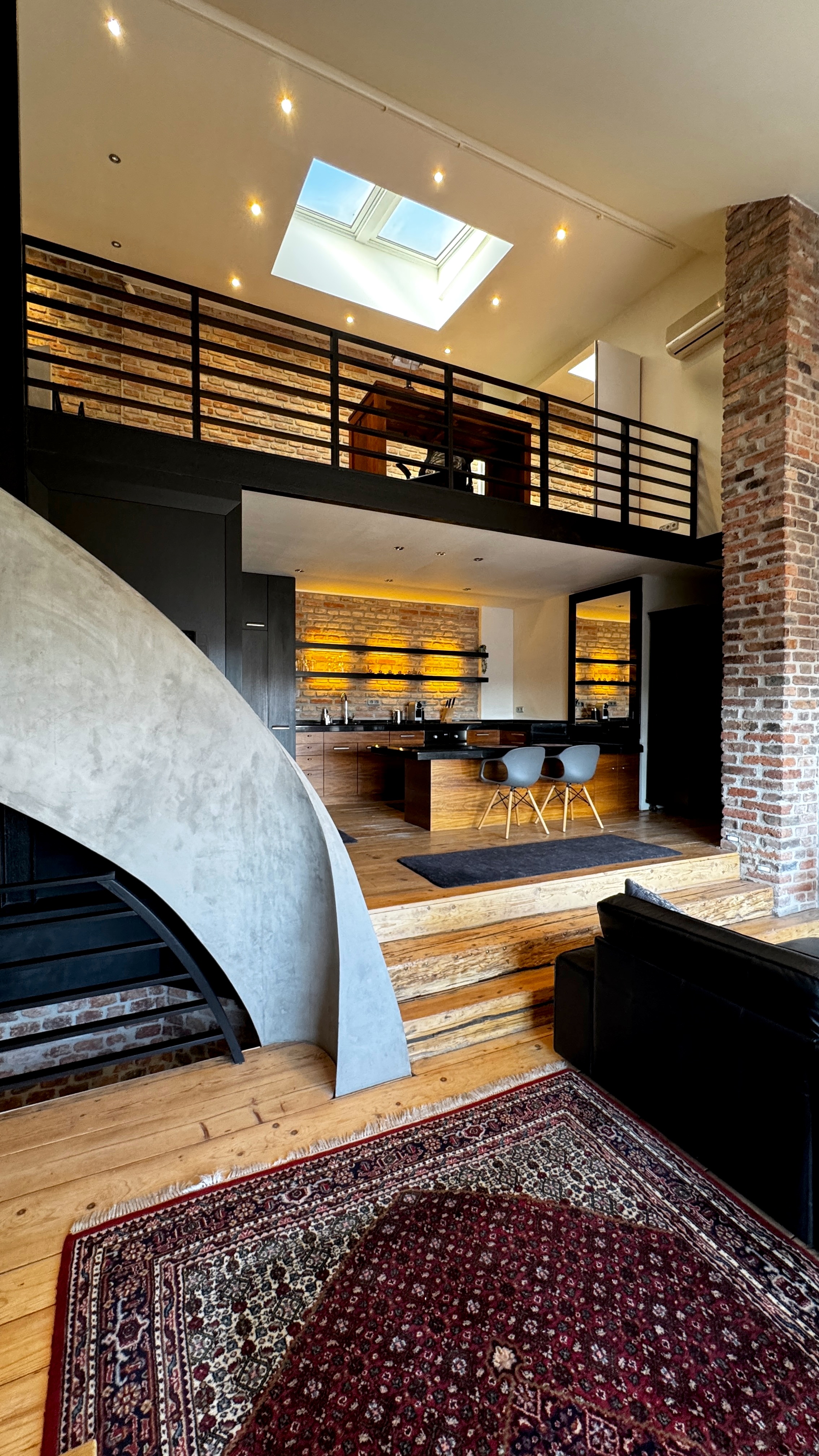 Dining area and kitchen atrium in a Prague luxury triplex with six-metre brick walls, mezzanine skylight, and massive timber flooring