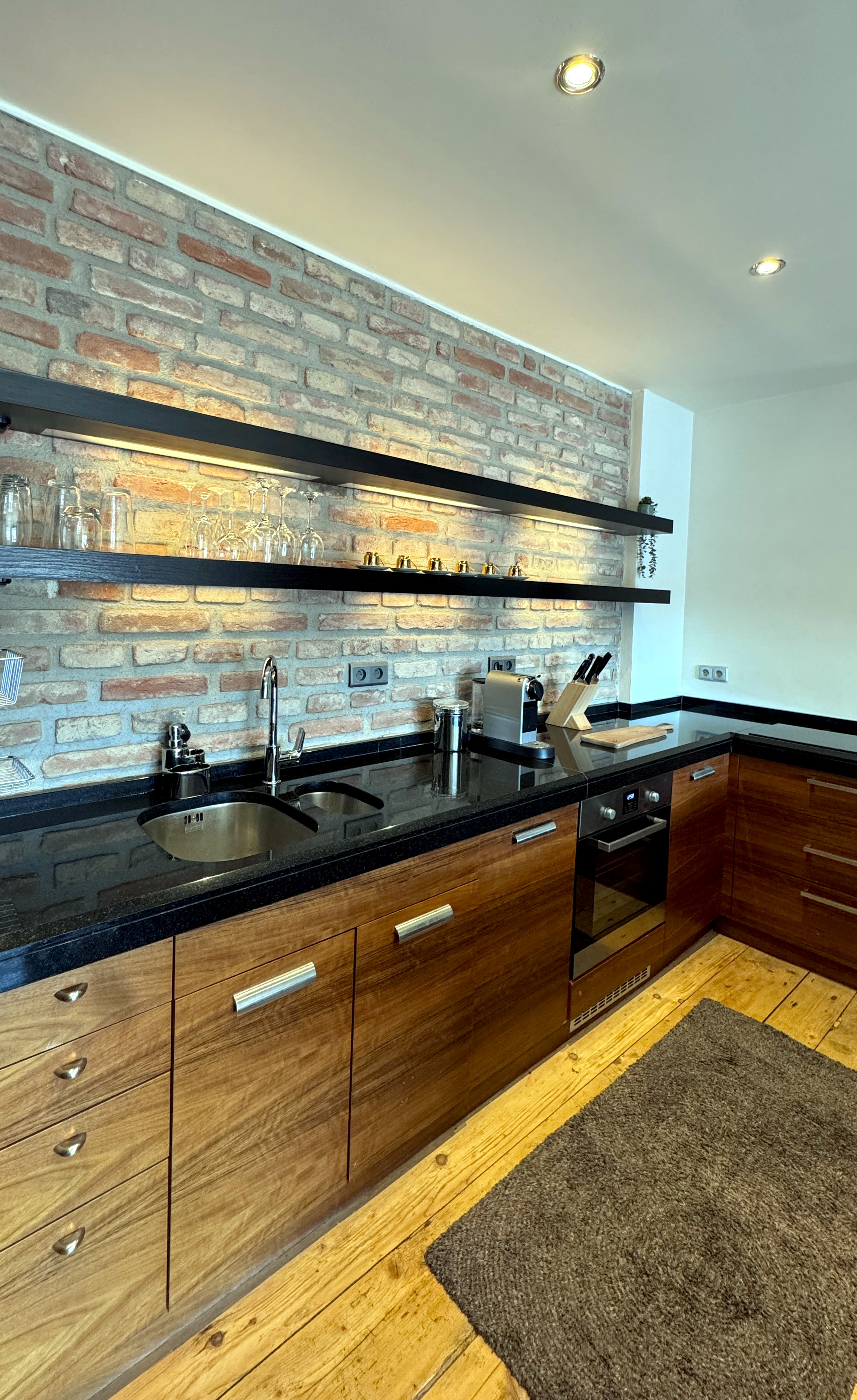 Artisan kitchen at Polska Penthouse featuring seamless black granite worktops, warm under-shelf lighting, and historic brick pillar detailing