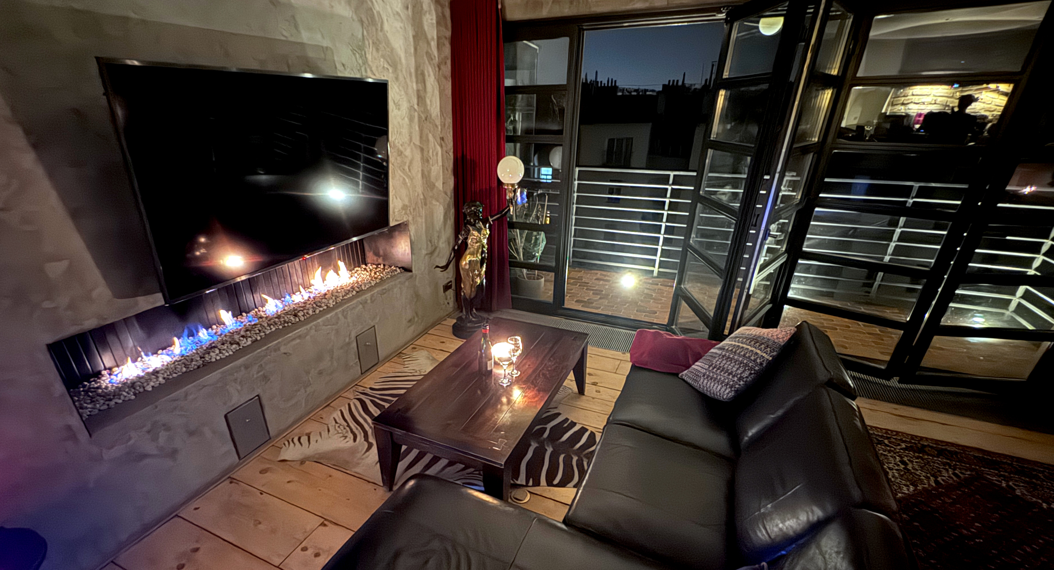 Evening mood at Polska Penthouse — minimalist wide-format gas fireplace set into a hand-finished concrete wall, with bifold doors open to the Prague night sky