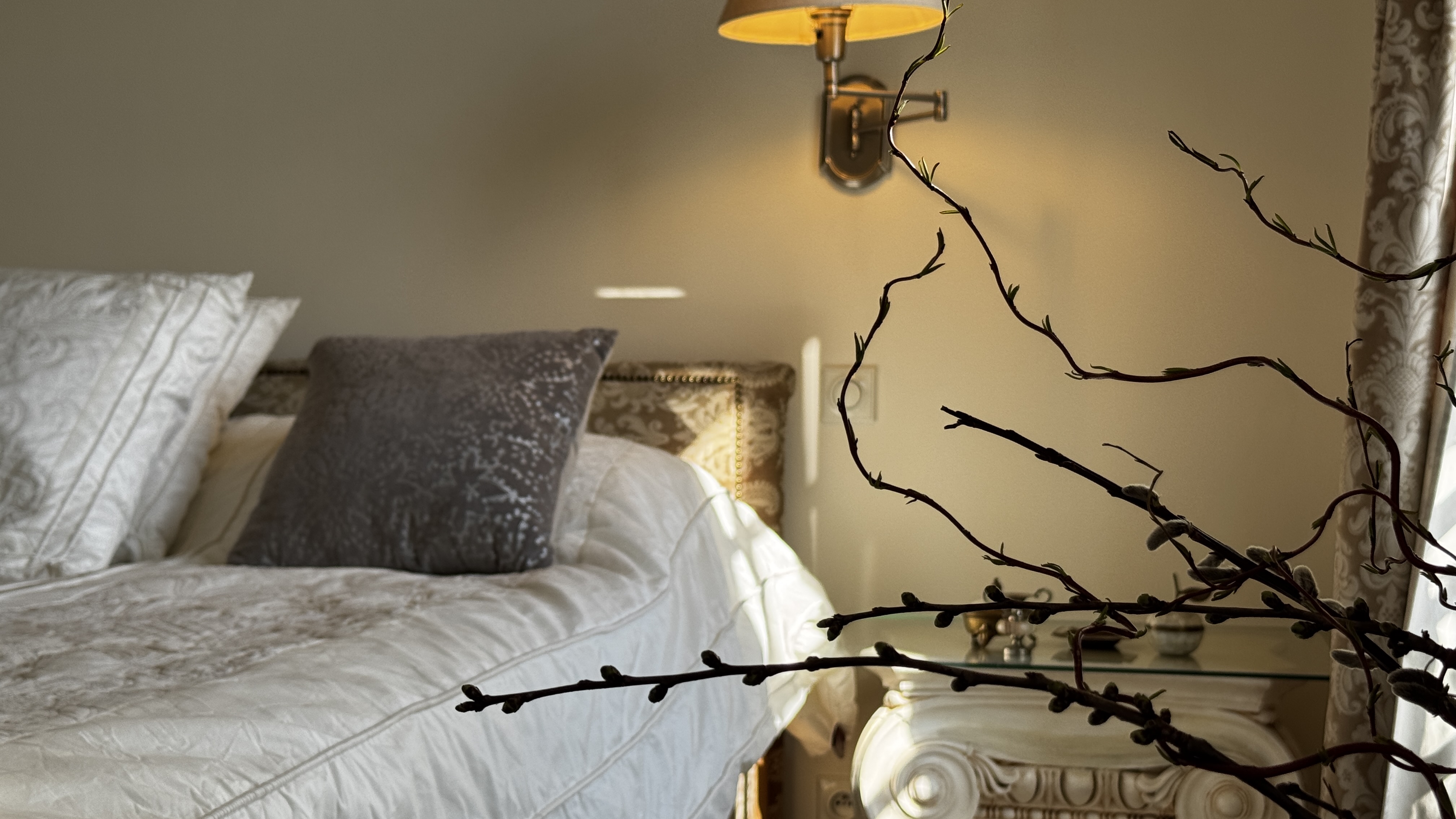 Intimate detail of the master suite at Polska Penthouse — bedlinens, velvet bolster, brass wall sconce, and a carved nightstand with bare branches