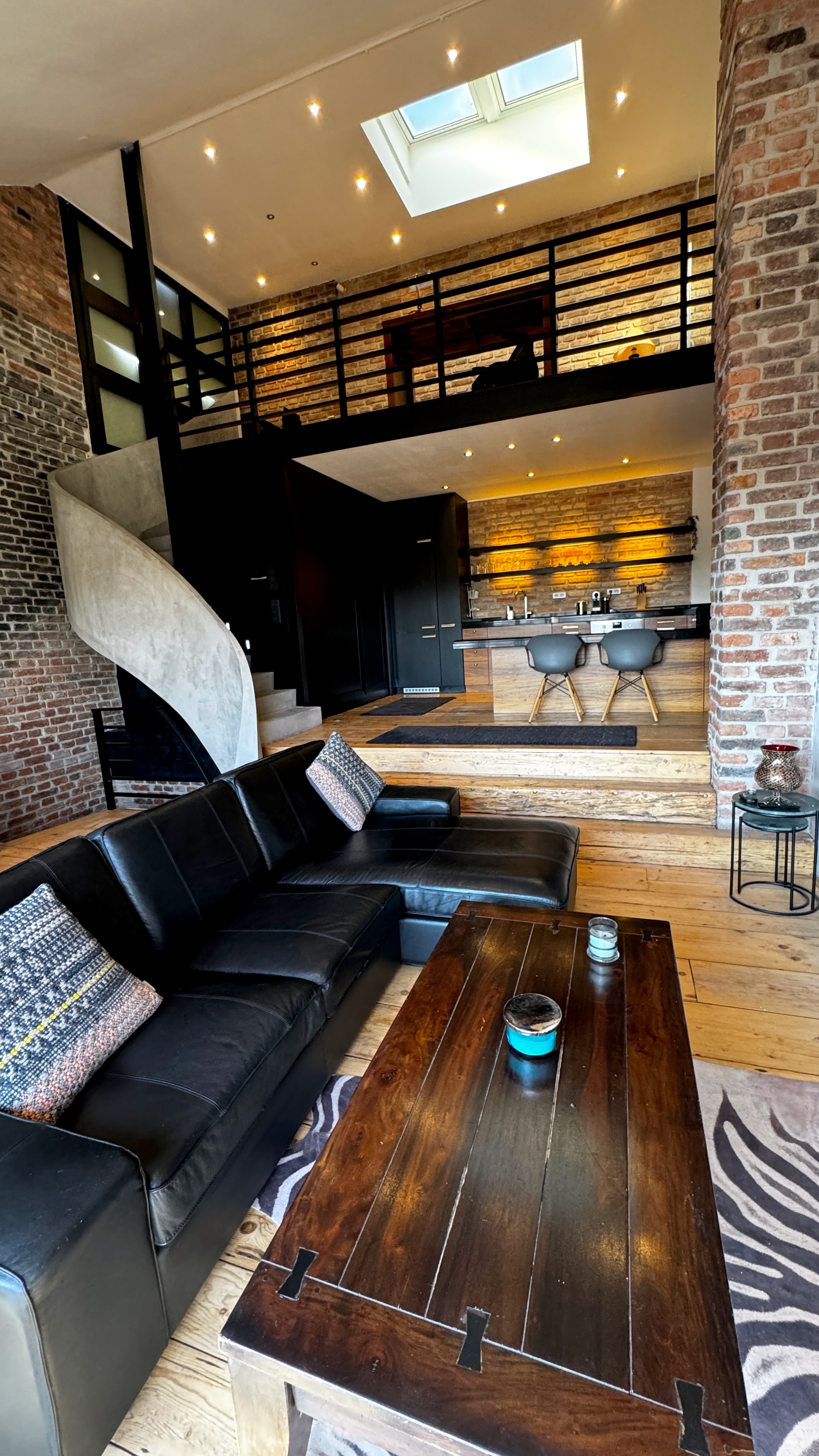 The Great Room of Polska Penthouse — a six-metre double-height atrium with original brick walls, mezzanine skylights, and massive timber floors in Vinohrady, Prague